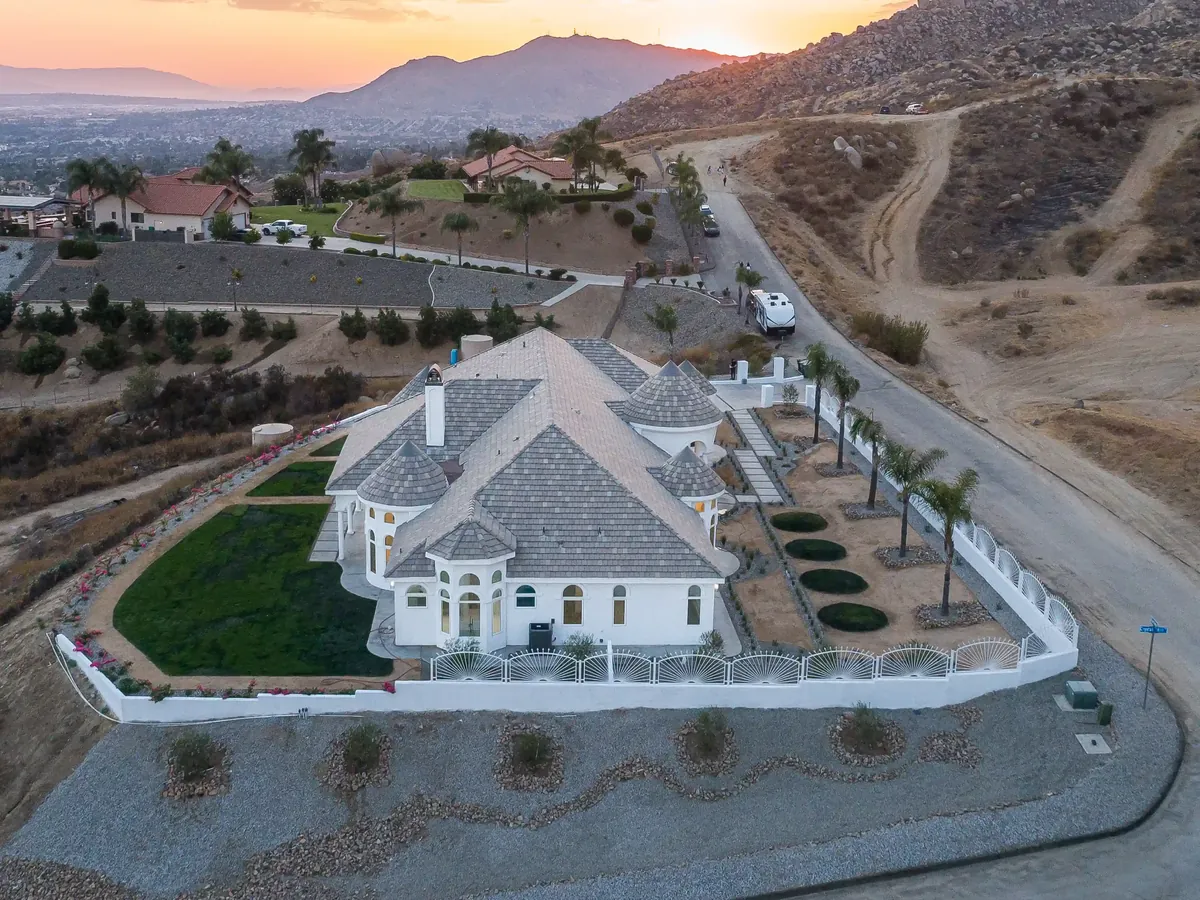 Home with a tile roof beside dry brush-covered hills at sunset